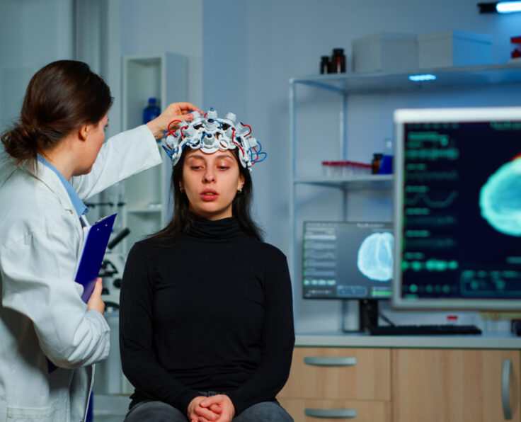 Neurological doctor cheking eeg headset explaining to patient diagnosis of disease and treatment for nervous system. Scientist researcher analysing brain scan and tomography on monitor in lab